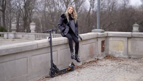 woman sitting on a wall with an electric scooter in a park