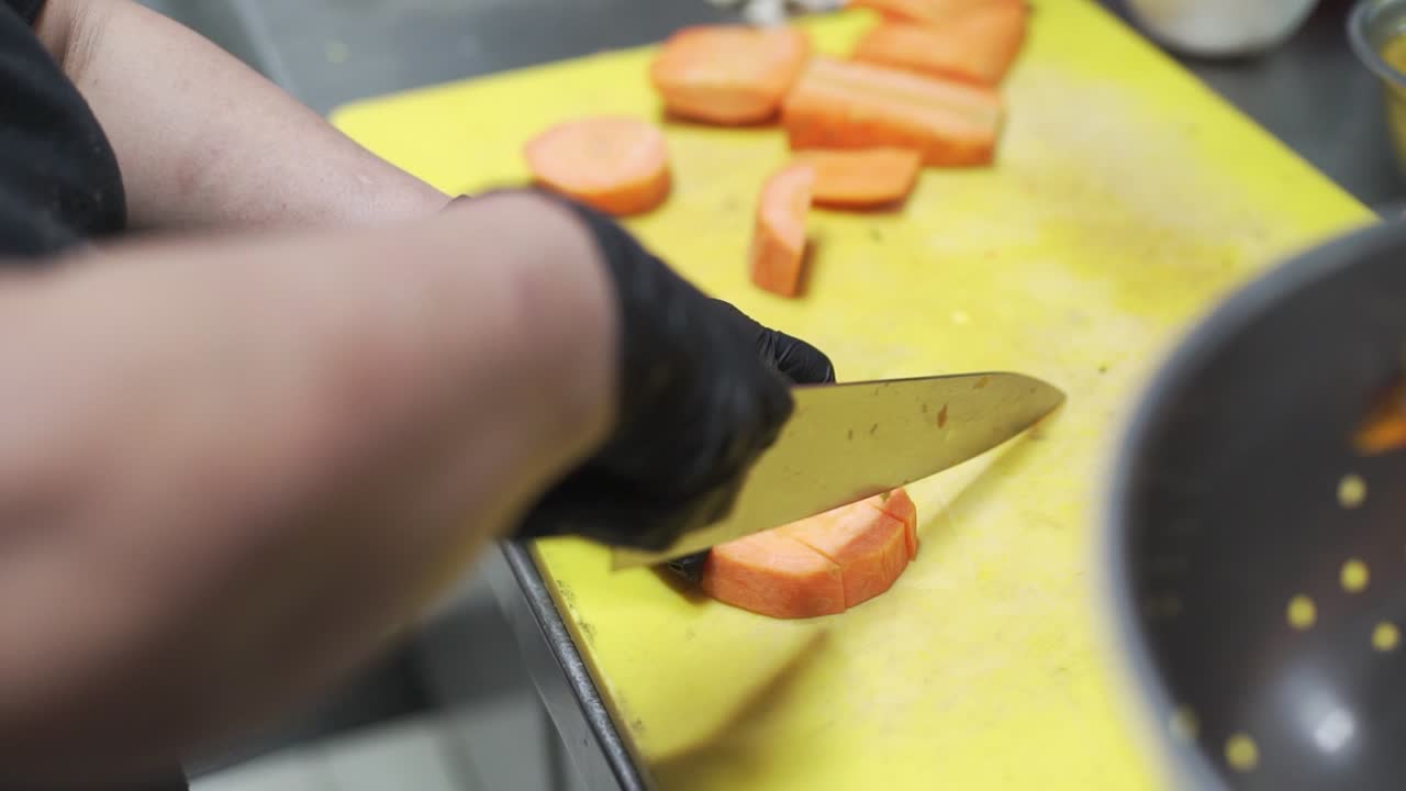 chef con guantes esterilizados negros cortando calabazas con un cuchillo afilado en una amplia tabla de corte amarilla