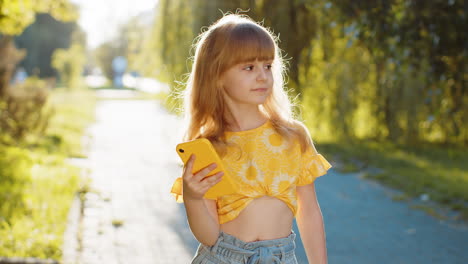 smiling girl in a yellow shirt looks at her phone in the park.