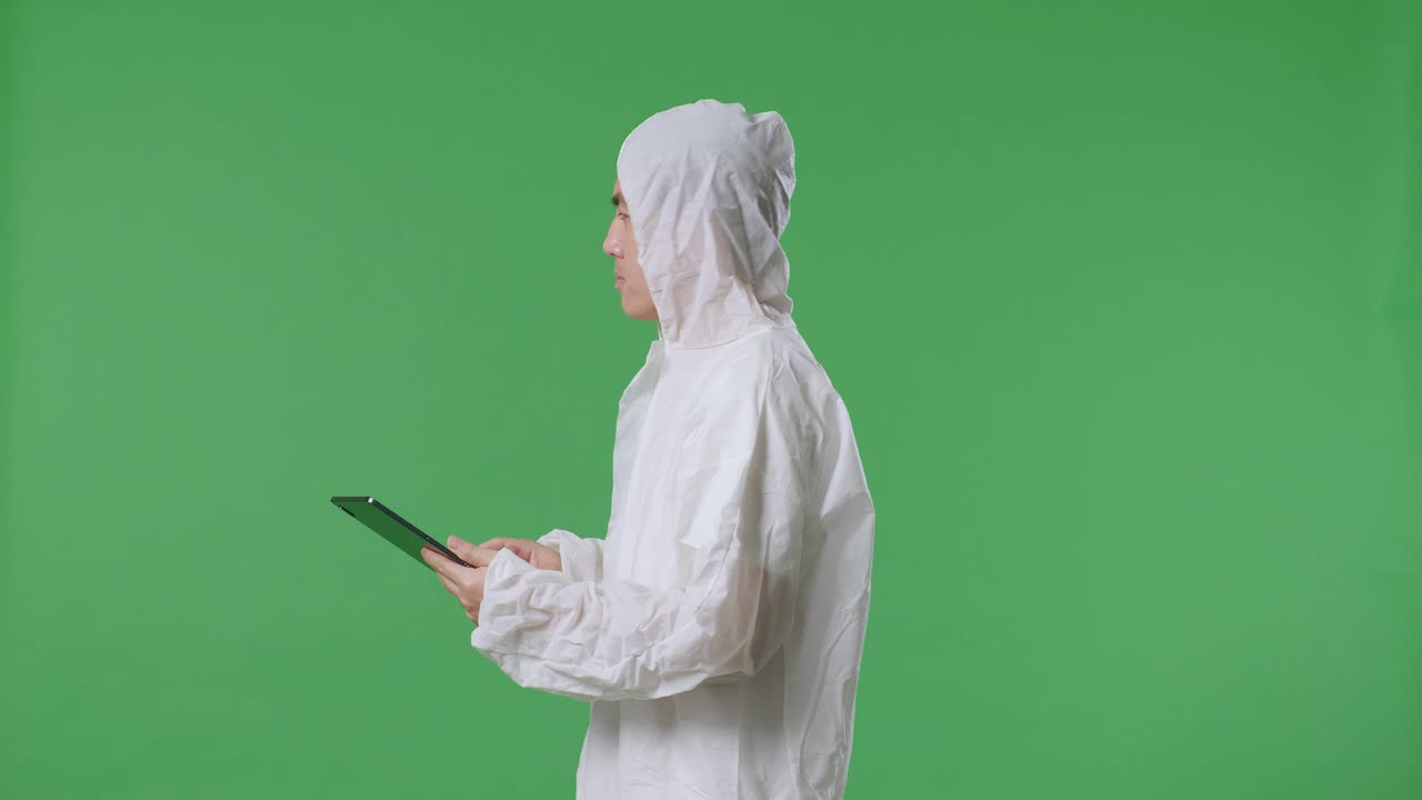 녹색 화면 배경에 서서 태블릿을 사용하는 아시아 남성 과학자의 측면 시각