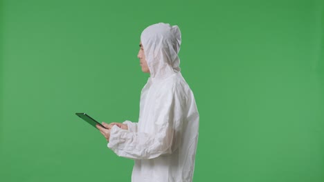 vista lateral de un científico masculino asiático usando una tableta y mirando a su alrededor mientras está de pie en el fondo de la pantalla verde