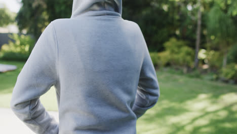 Rear-view-of-woman-in-white-hooded-top-in-sunny-garden-in-slow-motion-with-copy-space