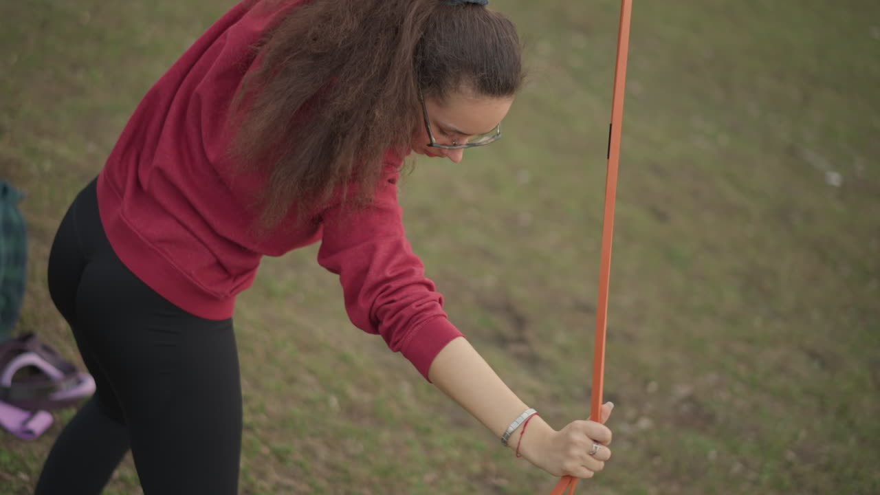 Coach Showcases Upper Body Mobility, Casual Park Workout With Orange Band, Individual In Athletic Gear Performs Shoulder Mobility Exercise With Orange Resistance Band In Park Setting