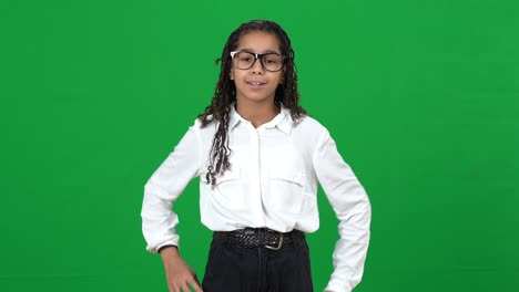 vista frontal de adolescente afroamericano adolescente nerd chica sacudiendo el dedo gestando en la pantalla verde y ajustando gafas. retrato de estudiante adolescente inteligente inteligente posando en el fondo chromakey.