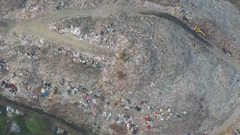 aerial view of a large landfill site with waste material and a yellow excavator