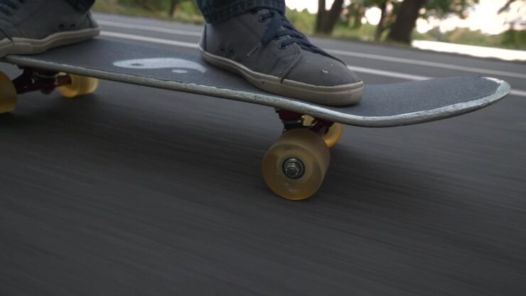Skateboard in discesa su una grande collina nel parco. La telecamera si muove davanti alla tavola più volte per un'inquadratura ad angolo interessante. Lago e vegetazione sullo sfondo.