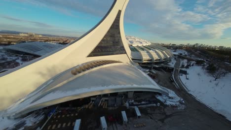fpv drone soars above snow-covered olympic stadium at sunset, creating a wintry aerial view