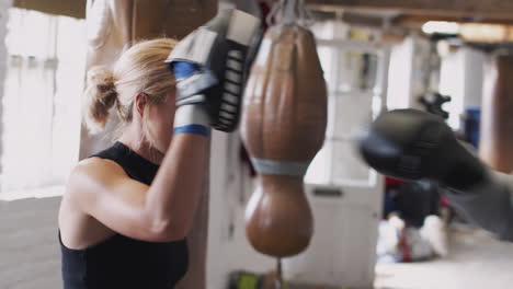 senior male boxer with younger female coach in gym using training gloves