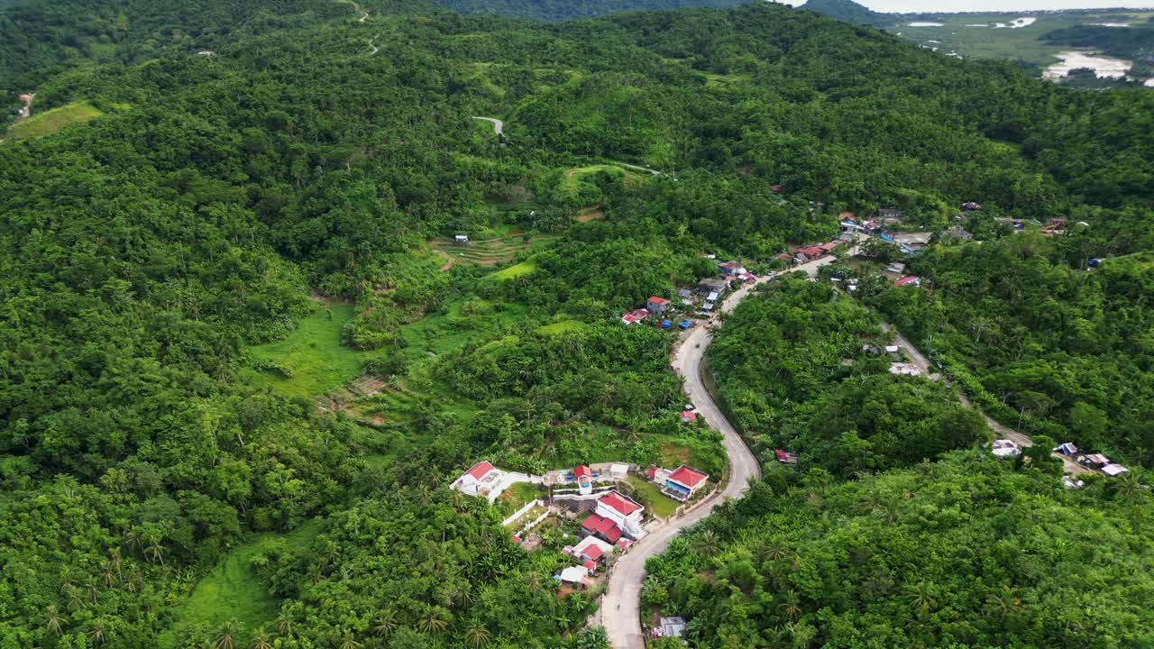 Stunning overview of rural barangay village amid lush tropical mountains at Catanduanes, Philippines - orbiting aerial view