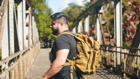 joven viajero con mochila caminando por el viejo puente oxidado al aire libre en un soleado día de verano