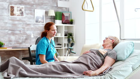 nurse in retirement home talking with an old lady lying in hospital bed