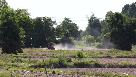 4K-Footage-of-Thai-Farmer-Driving-Tractor-Ploughing-Rice-Field-in-the-Distance-with-Dust-Blowing-Around-on-a-Hot-Day-in-Thailand