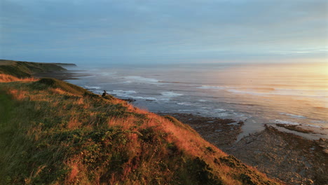 low rising establishing aerial drone shot of cleveland way in scarborough on misty morning at golden hour