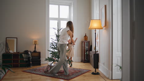 Smiling-mom-daughter-putting-garland-on-fir-tree-indoors.-Girl-helping-mother