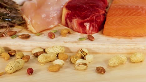 una variedad de alimentos ricos en proteínas, incluidas carnes, nueces y semillas, están artísticamente dispuestos en una superficie de madera