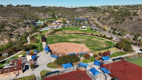 Vista-Aérea-De-Un-Campo-De-Béisbol-Y-Drones-Volando-Hacia-Atrás-A-Un-Campo-De-Fútbol-En-El-Parque-Alga-Norte,-Carlsbad,-California