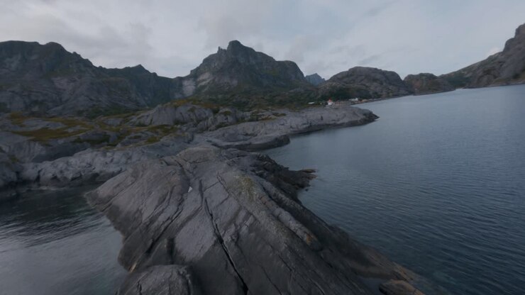 Volando sopra le rocce sulla costa di Nusfjord, Lofoten, osservando Nusfjord e le montagne sullo sfondo al rallentatore