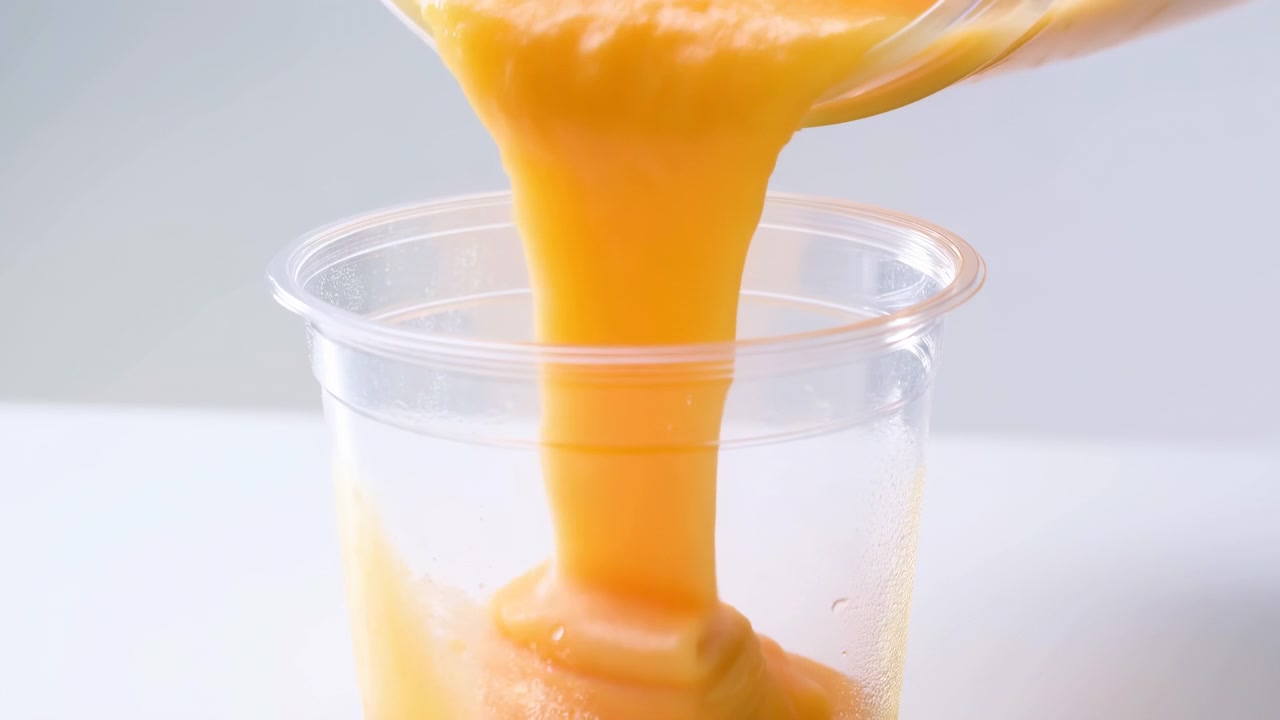 Sfondo neutro con sovrapposizione di testo, prospettiva dall'alto di liquido arancione versato in un bicchiere di plastica trasparente. Dimostrazione di prodotto alimentare commerciale in un ambiente pulito e dall'atmosfera neutra.