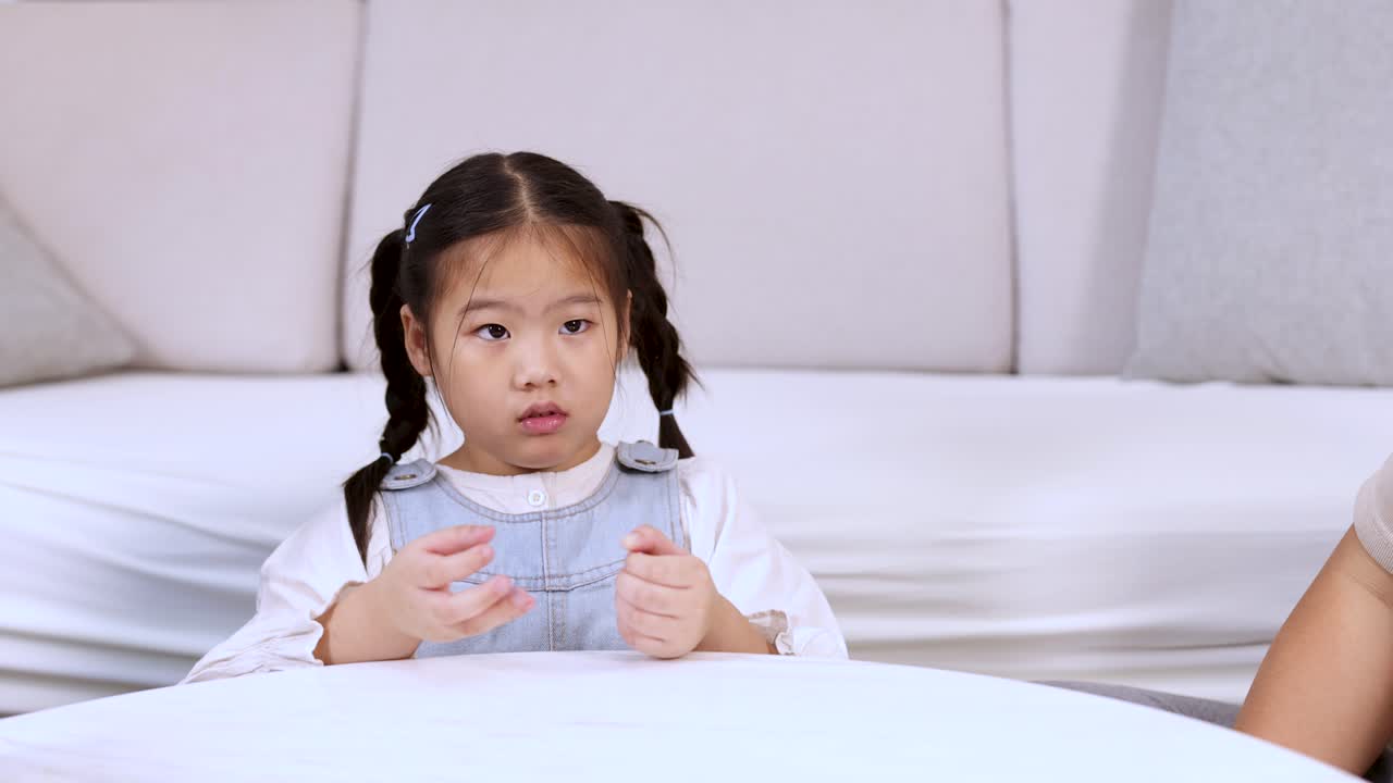 Little girl tosses toy egg on table, parent nearby, bright indoor lighting, playful learning moment