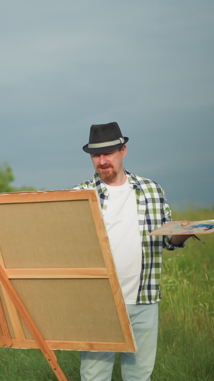 A painter holding a palette and brush captures the image of a woman in a white dress and hat, standing poised in front of him. Set in a lush grassy environment