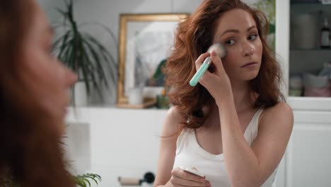 mujer pelirroja haciendo maquillaje en el baño.