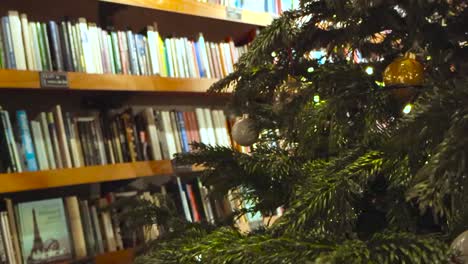 Beautifully decorated Christmas tree in front of vintage books and magazines in a library or bookstore called READ in Tallinn Estonia during holidays. The tree is decorated with golden glossy balls.