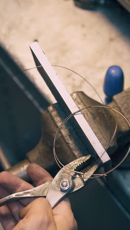 cu: young jeweler pulls long thin gold wire through tool fixed with bench vise clamp in workshop close upper view