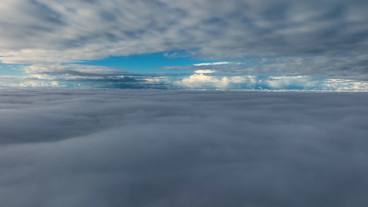 vista aérea entre capas de nubes que parece casi navegar sobre el océano, con cielo azul y nubes blancas en la distancia