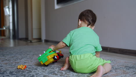 one year old toddler plays with a toy car at home. rear view of a child having fun.