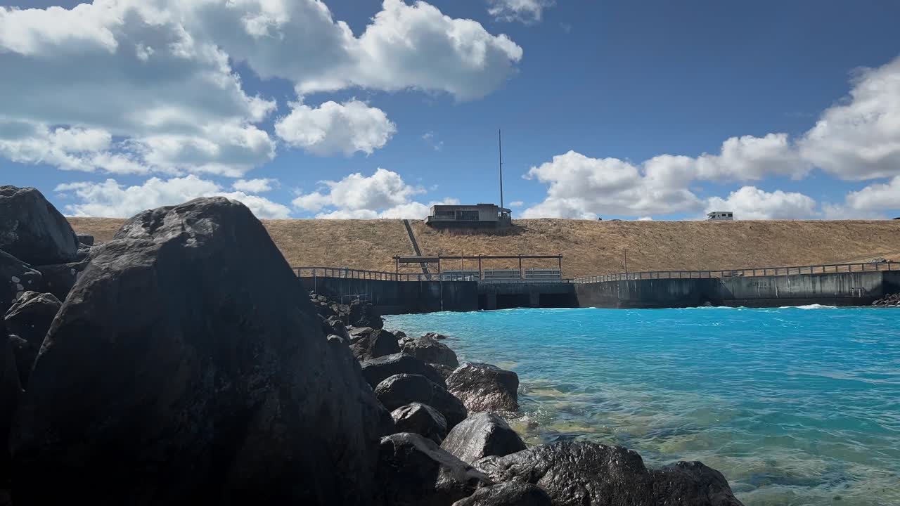 Vehicles driving over dam over pukaki hydro canal on sunny day in New Zealand
