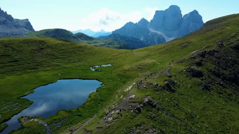 Toma-Aérea-De-Corredores-Corriendo-En-Dolomitas-Cerca-Del-Tranquilo-Lago-Azul,-Italia