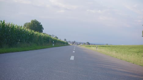 Tilted-right-angle-of-slow-moving-down-european-road-near-large-corn-field-during-golden-sunrise-in-Switzerland