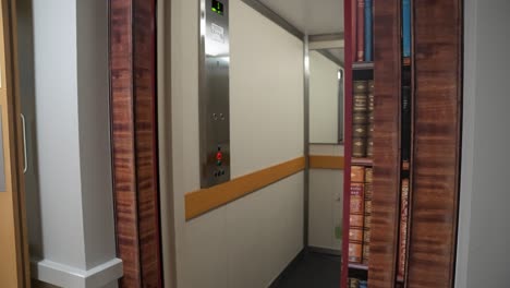 Hidden-elevator-door-way-concealed-and-revealed-by-use-of-fake-bookcase-using-vinyl-sticker-art-to-hide-the-door-inside-building-as-the-door-opens