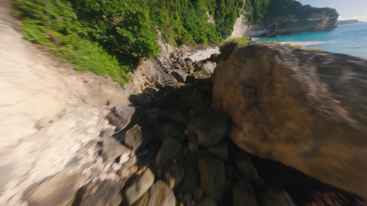 Ripresa FPV in slow motion sopra le rocce e la spiaggia tropicale sabbiosa a Bali in una giornata di sole.