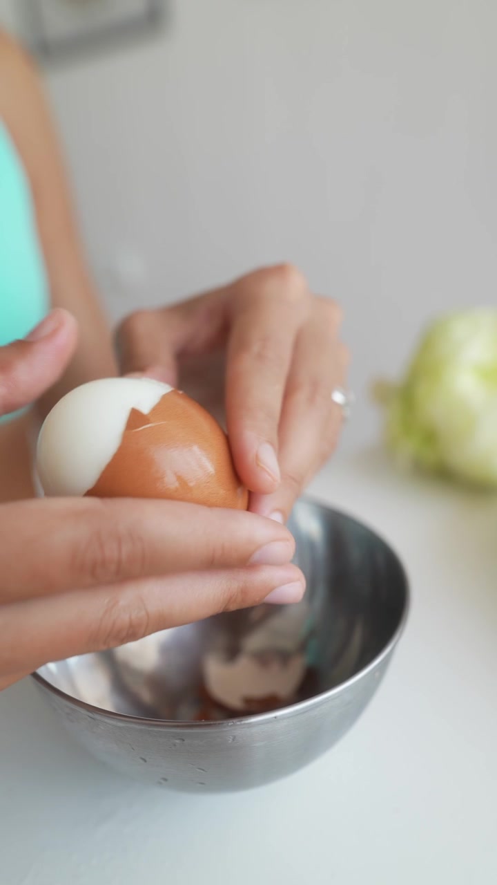 Woman Peeling a Hard Boiled Egg into a Metal Bowl