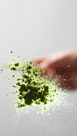 close-up of a hand sprinkling green glitter, freeze-frame effect on a light background