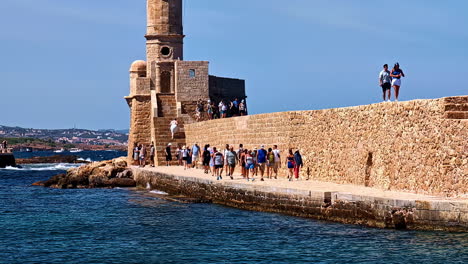 tourists walking on a stone wall near a lighthouse in crete, greece