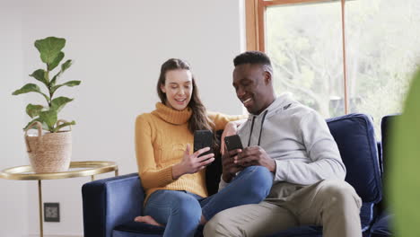 happy diverse couple sitting on sofa, using smartphone and credit card in home,copy space