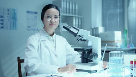 portrait of female scientist working with microscope at desk in laboratory