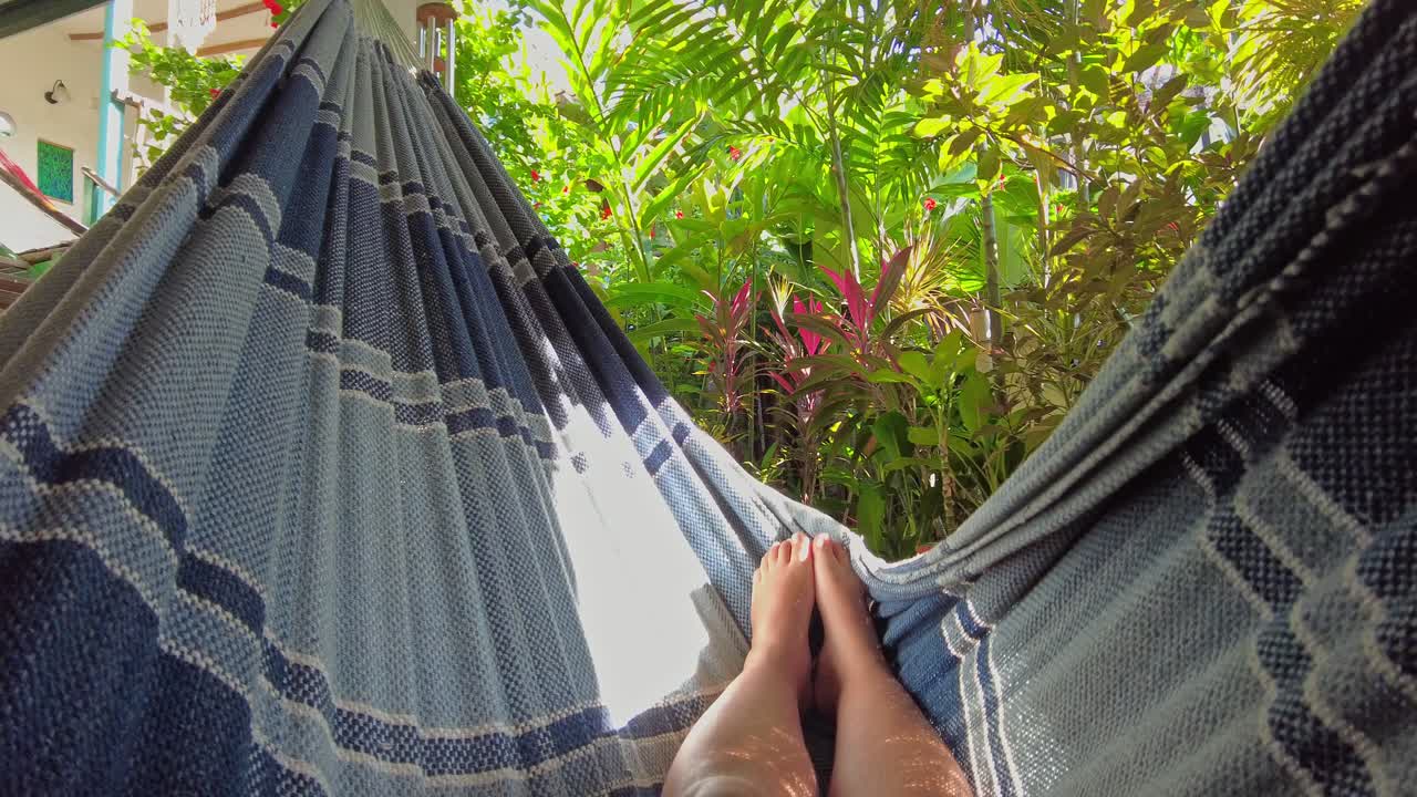Toma POV que los muestra balanceándose en una hamaca con vistas a un exuberante jardín verde en una propiedad de alquiler en el pueblo costero de Choroní, Aragua, Venezuela