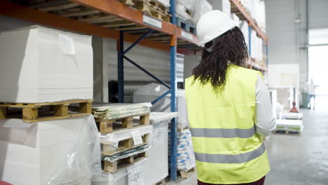 back view of an african american female worker in helmet counting goods in stock