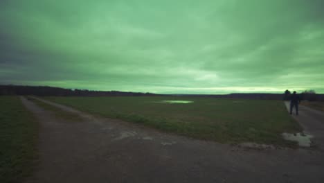 modern black swordsman warrior awaiting battle opponent in open field under green sky, europe, 4k | muscular, intimidating, shadow, figure, blurry, dark clothes, powerful, alien, invasion, guarded