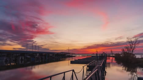 Fire-red-orange-glow-spreads-in-sky-and-clouds-above-empty-boat-dock-and-harbor,-time-lapse