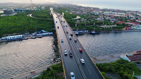 drone ascends as cars drive over queen juliana bridge with tug boats docked below in river