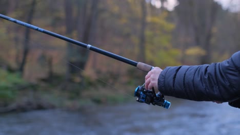 a fisherman holding a rod for catching predatory fish and turning the handle of the reel that is a fisherman holding a rod for catching predatory fish and turning the handle of the reel that is wound on the fishing line a man catches fish in a mountain river