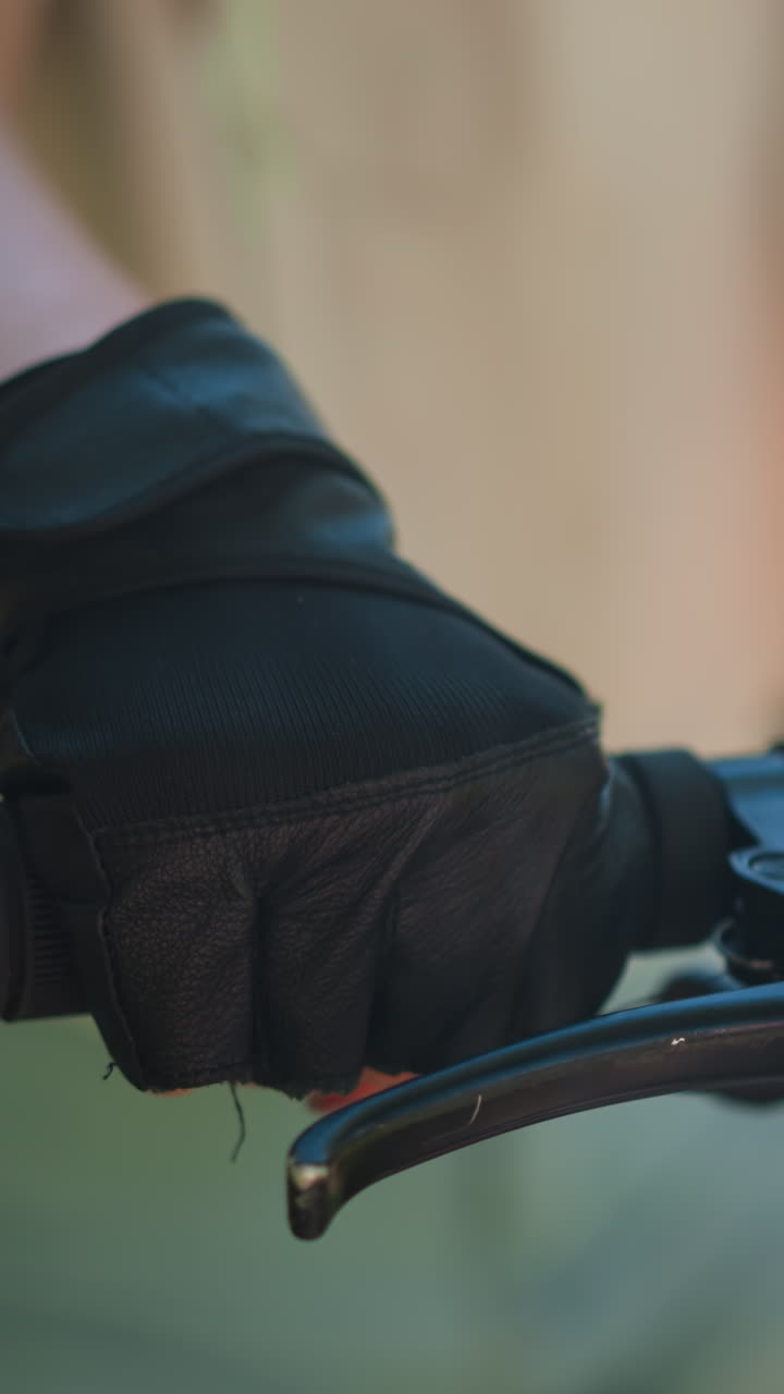 primer plano de un individuo agarrando el manillar de la bicicleta, acelerando y sosteniendo el freno con la mano con guante, mostrando el control y el enfoque en la actividad de ciclismo, el fondo suavemente borroso con vegetación