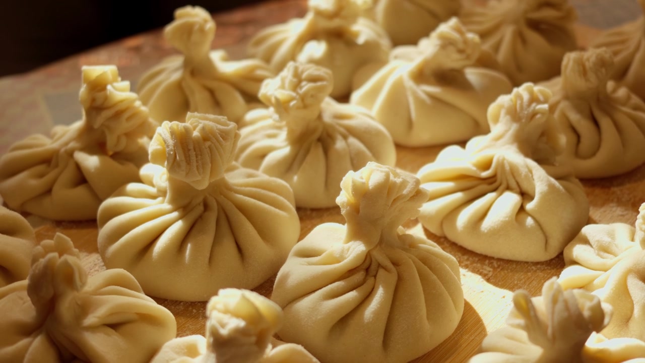 Slow camera movement across rows of fresh uncooked Georgian khinkali dumplings resting on rustic wooden board in soft side light, capturing authentic Eastern European culinary heritage.
