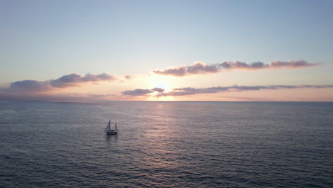 Die-Ruhe-Eines-Ruhigen-Ozeans,-Während-Ein-Segelboot-Anmutig-Durch-Die-Schillernden-Farben-Eines-Ruhigen-Sonnenaufgangs-Segelt,-Umrahmt-Von-Einer-Wolkenlinie,-Während-Sanfte-Wellen-Eine-Faszinierende-Atmosphäre-Schaffen