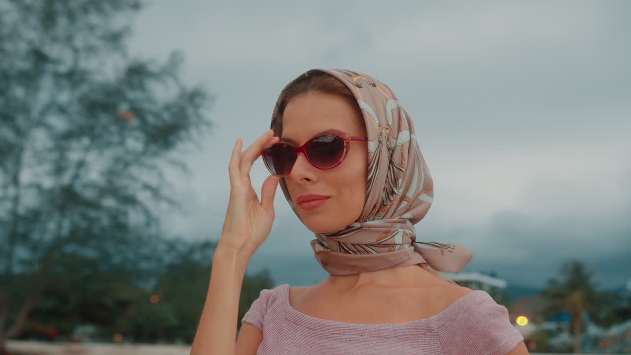 A woman wearing a scarf and sunglasses outdoors on a cloudy day