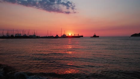 sunrise over santa marta, colombia: vivid sky reflects on a bay with sailboats, yachts, and industrial ships. a mix of leisure and commerce in a colorful, awakening caribbean port.